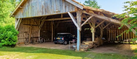 A rustic barn with a covered entrance, a car parked inside, and a bicycle leaning against the wall.