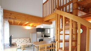 Un interior de madera con una escalera, una cocina y una sala de estar con sofá y mesa.
