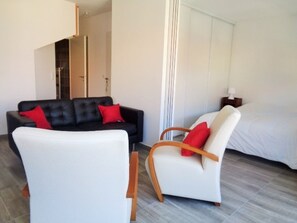 Una habitación de hotel moderna con un sofá de cuero negro, un sillón blanco y una cama.