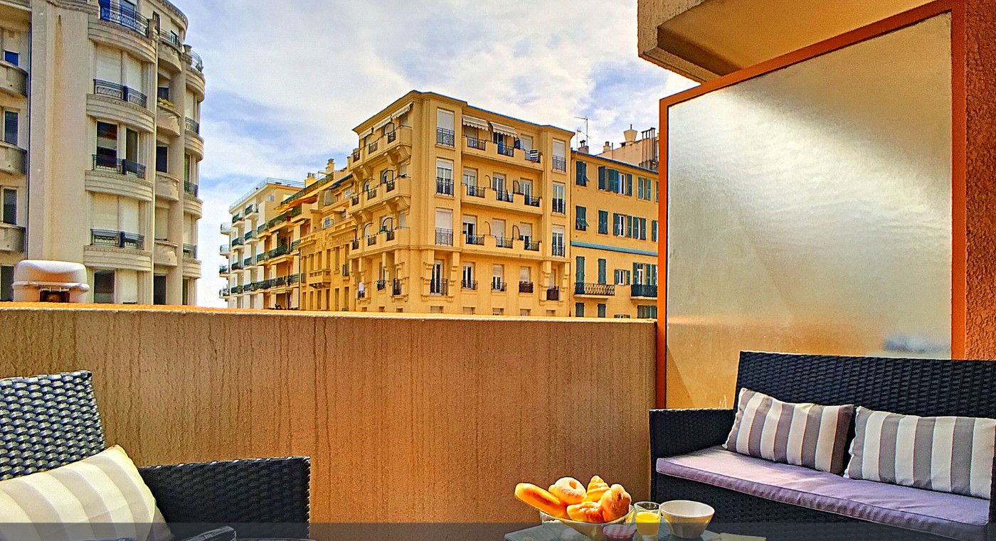 Un balcón con mobiliario de mimbre, una mesa de vidrio y vista a un edificio amarillo.