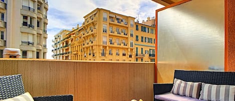 En balkon med fletningsmøbler, et glasbord og udsigt til en gul bygning.