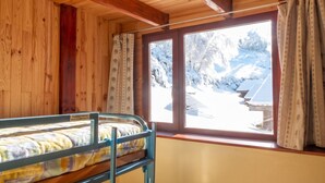 Ein Zimmer in einer Holzhütte mit einem Etagenbett, einem Fenster mit Vorhängen und Blick auf eine verschneite Landschaft.
