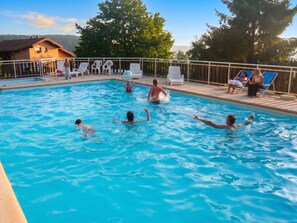 A swimming pool with people in the water, surrounded by lounge chairs and a wooden deck. - Homerez - Chalet in Le Tholy (Le Tholy)