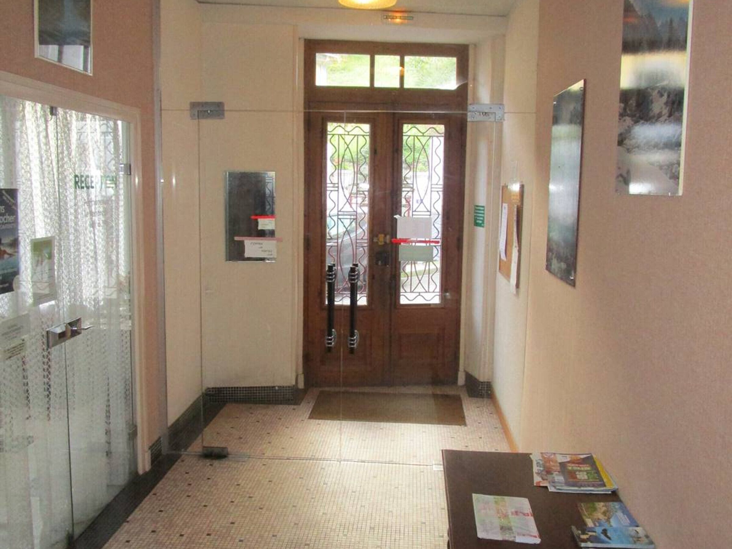 A hallway with a wooden door, a glass door, and a tiled floor.