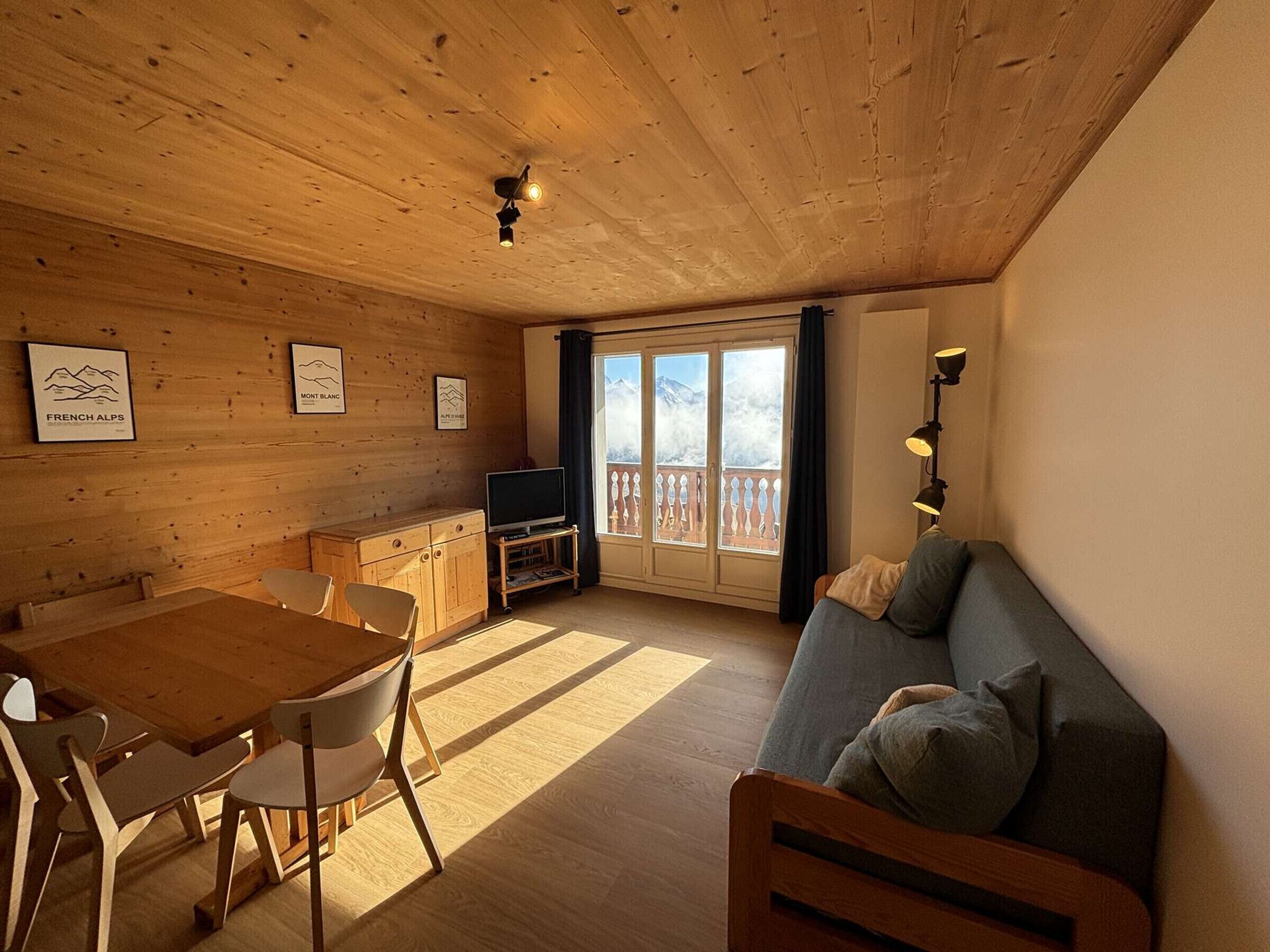 A cozy cabin interior with a wooden dining table, chairs, a sofa, and a TV.
