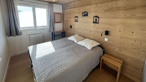 Quarto com teto de madeira, cama com colcha acolchoada, mesa de cabeceira e janela com cortinas.