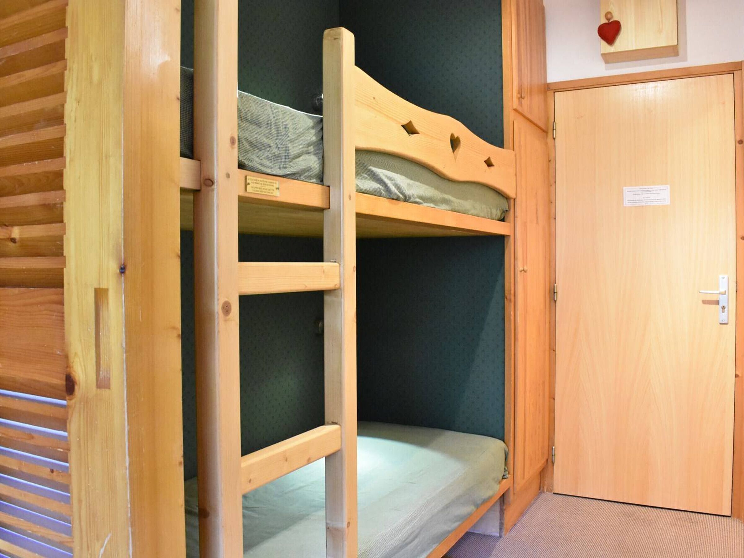 A bunk bed with a green mattress, a wooden door, and a heart-shaped decoration on the wall.