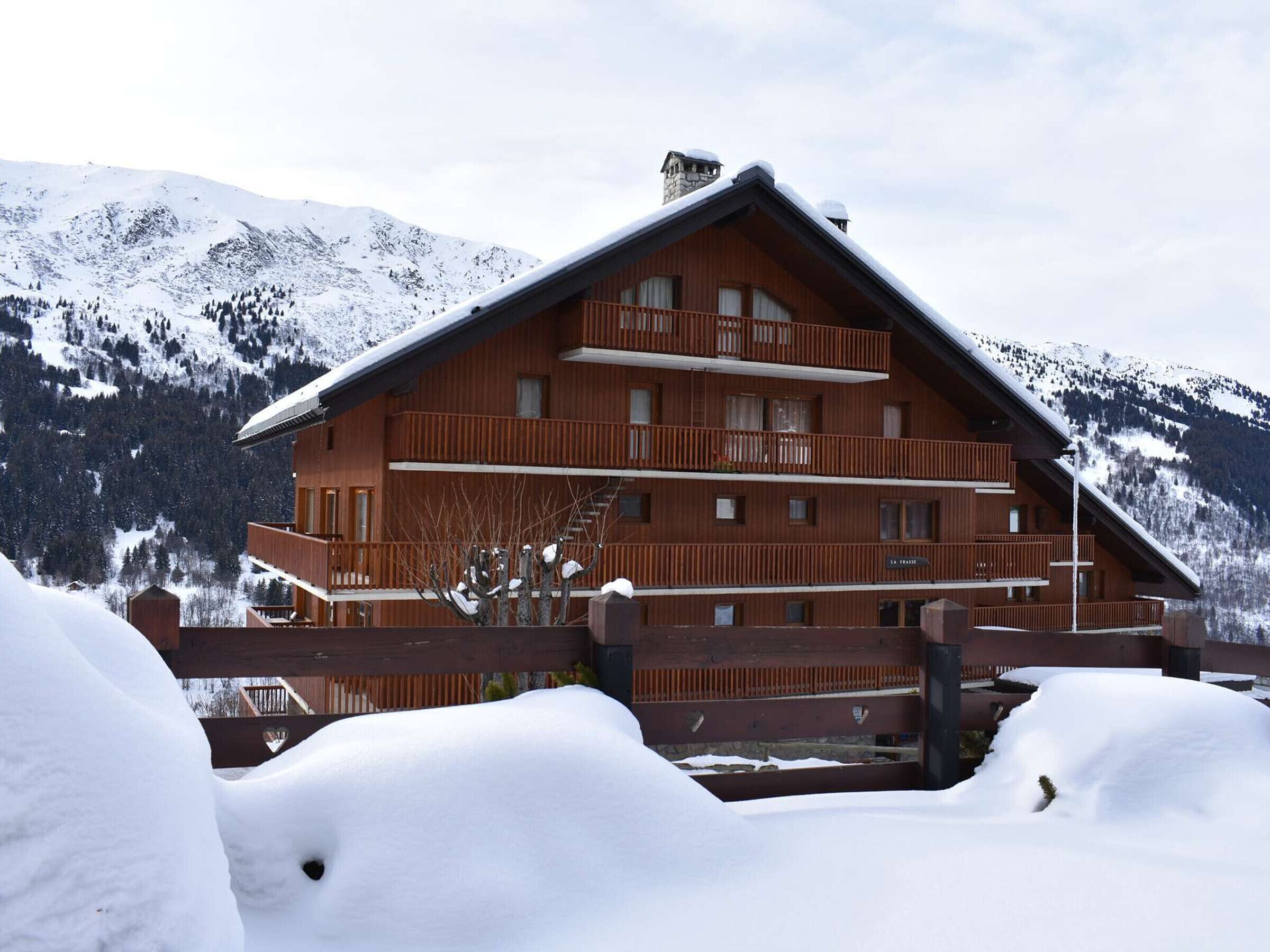 A multi-story wooden lodge with balconies, set against a snowy mountain backdrop.
