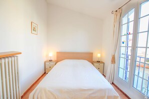 A bedroom with a bed, bedside tables, a radiator, and a window with curtains. - Close to the center 4 persons house  et  15m mooring (PORT GRIMAUD)
