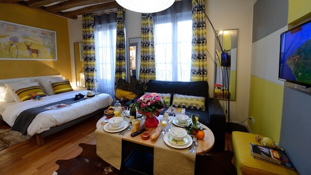 A cozy hotel room with a bed, a dining table set with breakfast, and a large window with curtains. - A2DF Boogie-Woogie (París)