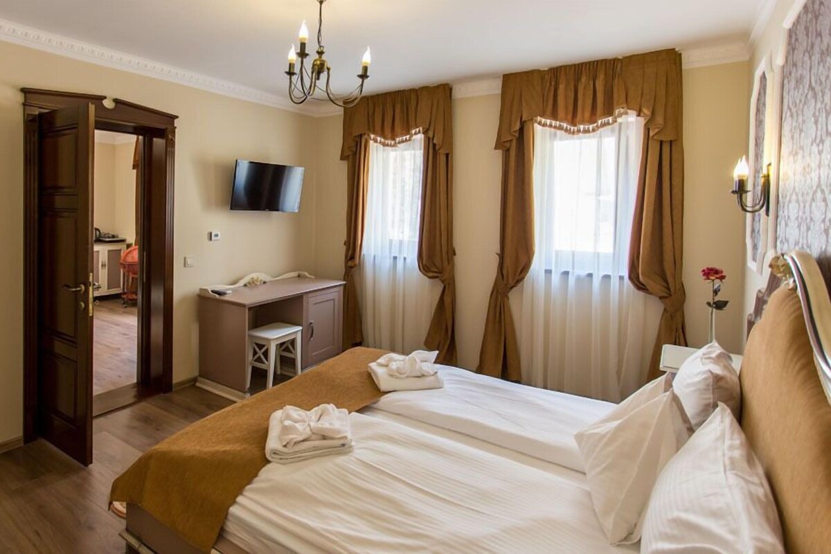 A hotel room with a bed, desk, chair, TV, and curtains.