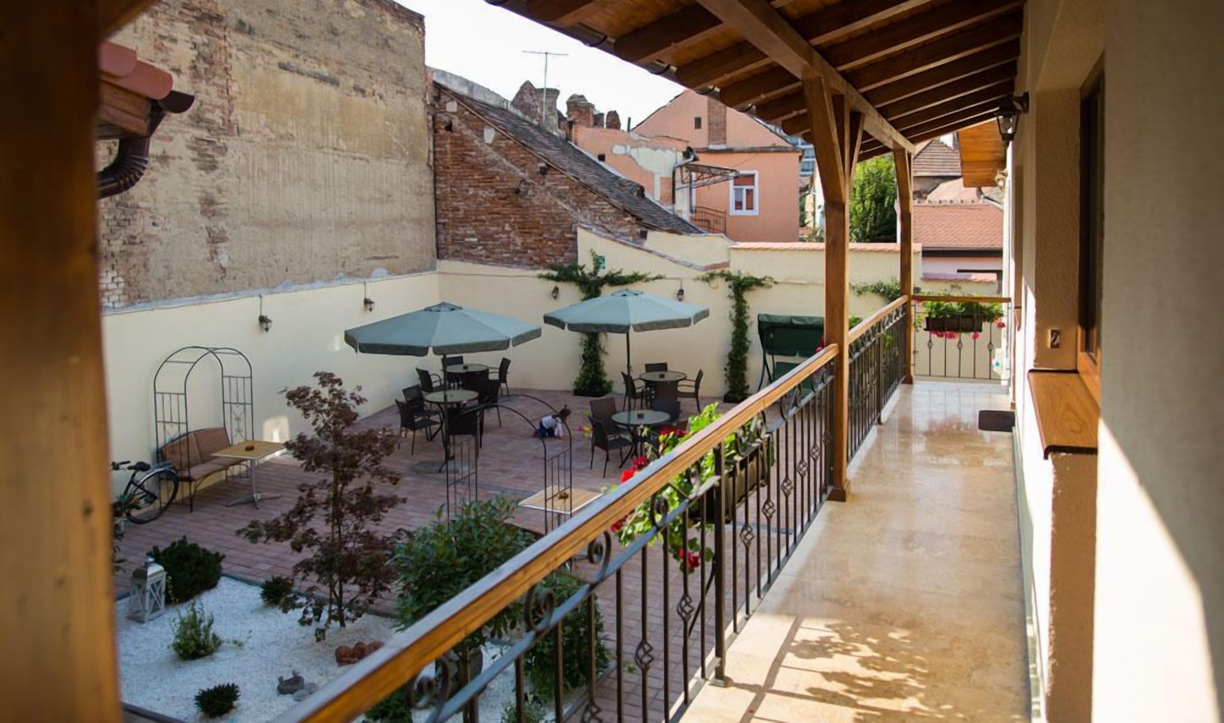 A covered outdoor patio with tables and umbrellas, a brick wall, and a wooden railing.