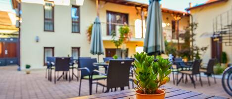 Un espace extérieur aménagé avec des tables et des chaises en bois, une plante en pot et des parasols.