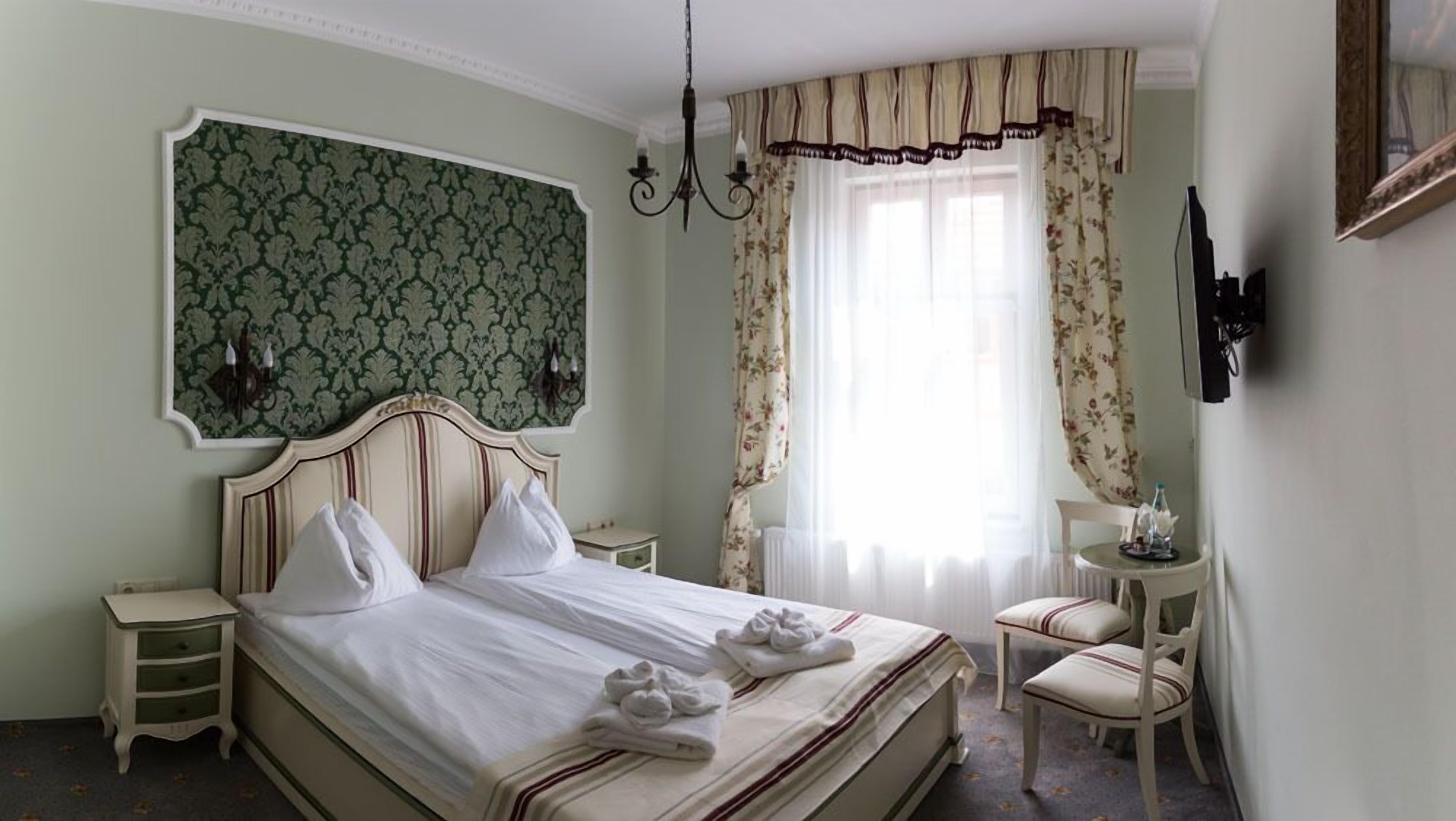 A neatly arranged hotel room with a bed, two bedside tables, a chair, a desk, and a large window with curtains.