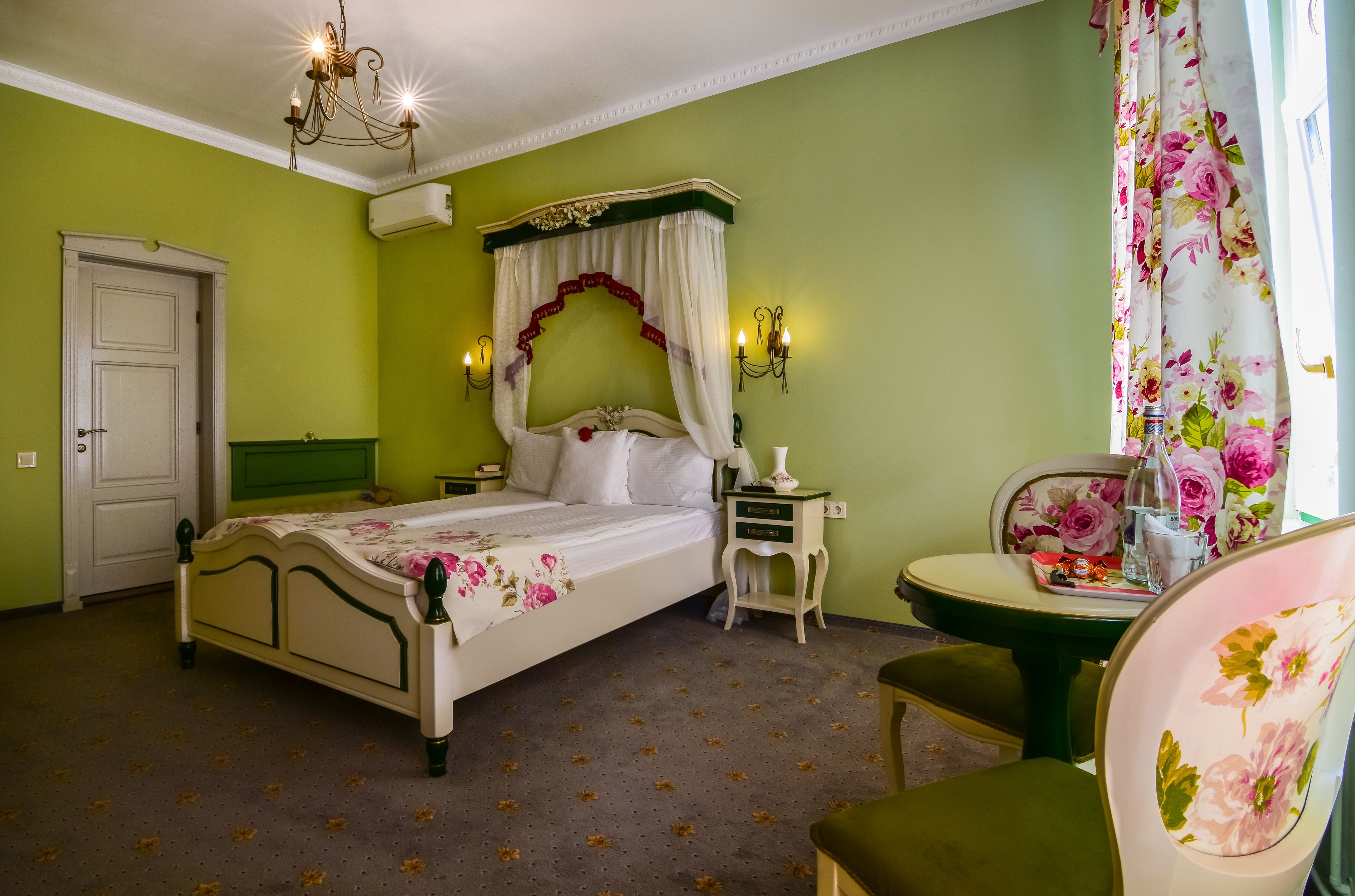 A bedroom with a four-poster bed, a nightstand, a chair, and a table with a floral tablecloth.