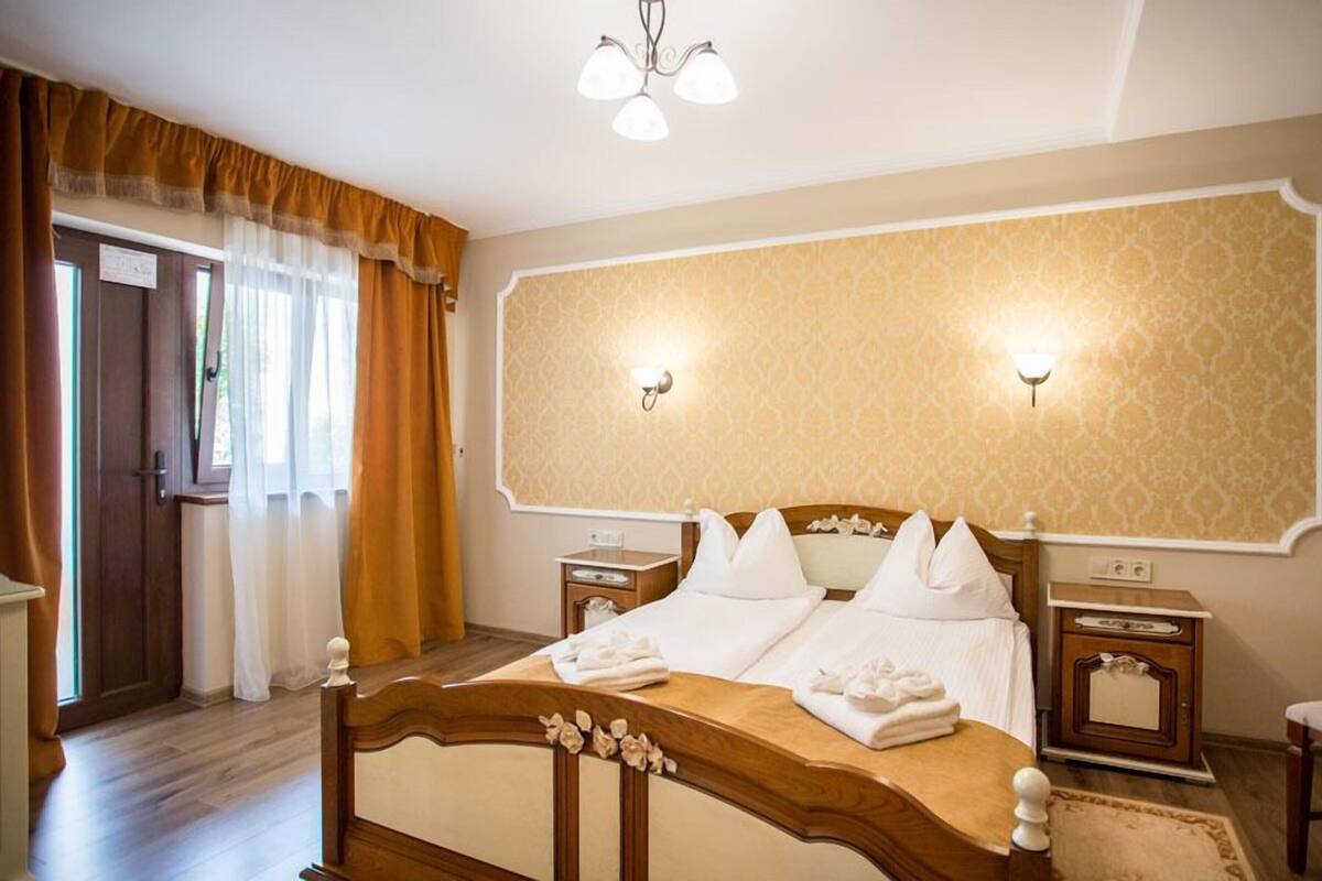 Una habitación de hotel con una cama de madera, dos mesitas de noche, un espejo y una araña.
