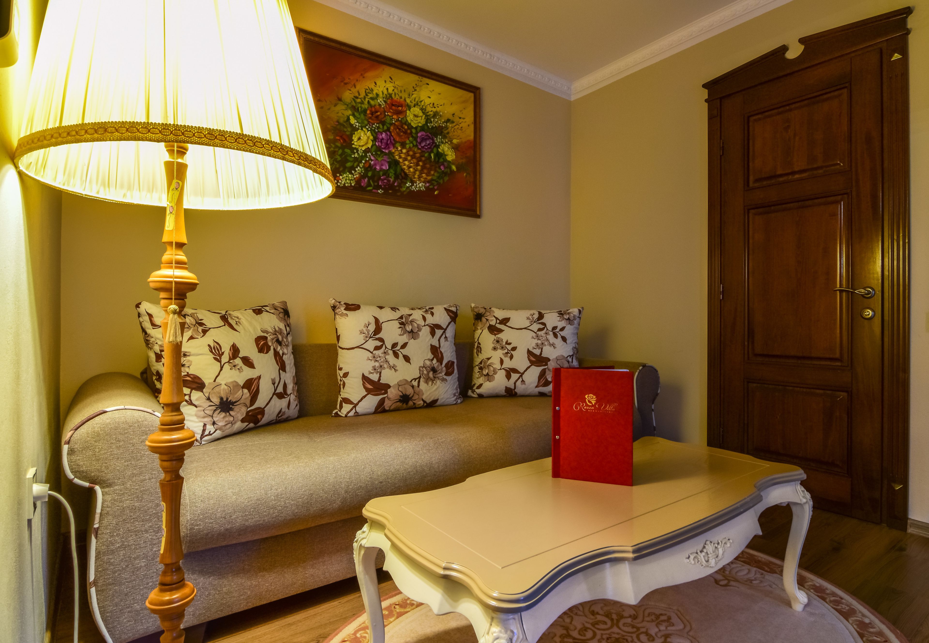 A living room with a sofa, a table, a lamp, a painting, and a door.