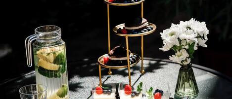 A three-tiered dessert stand with cupcakes and berries, a glass pitcher with a mint garnish, and a vase of white flowers on a table.