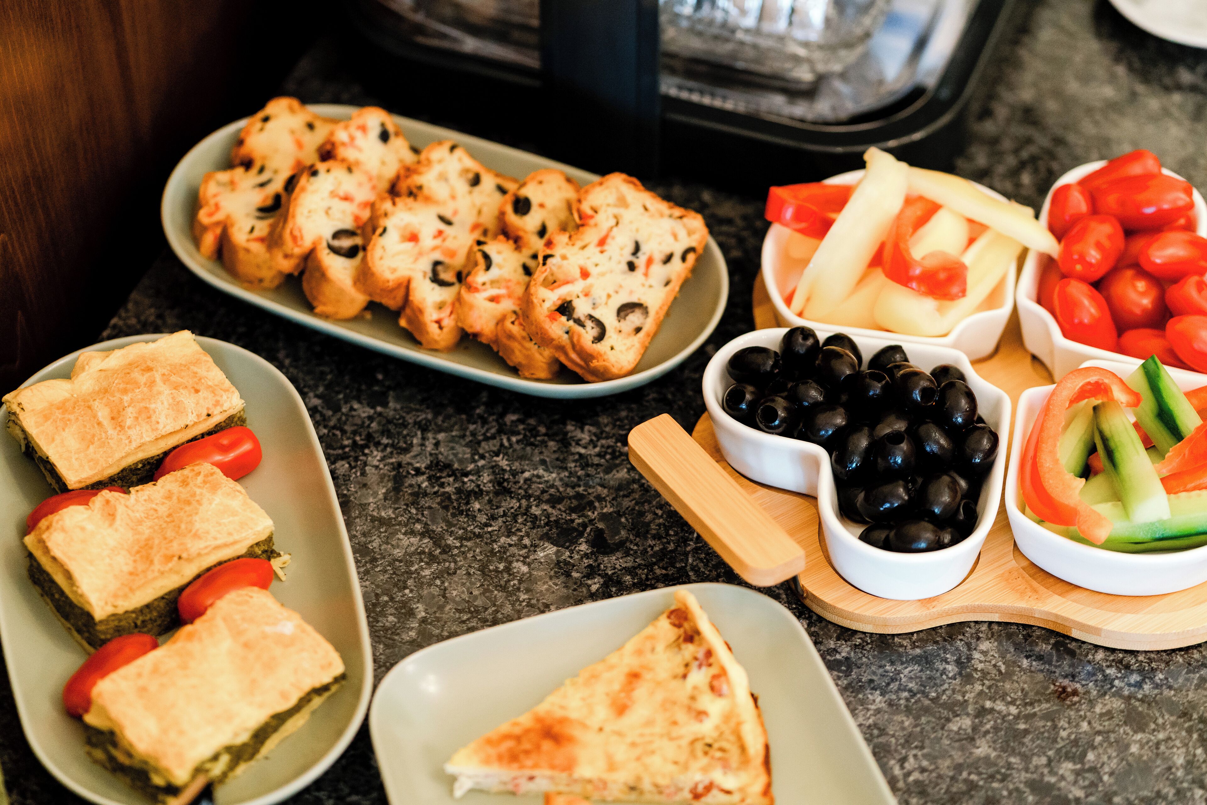 A variety of food items including bread, tomatoes, olives, and sliced vegetables on a countertop.