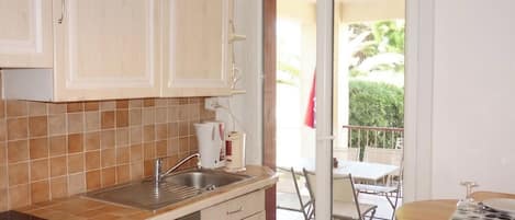A kitchen with a built-in dishwasher, a sink, and a window leading to a balcony with a table and chairs.