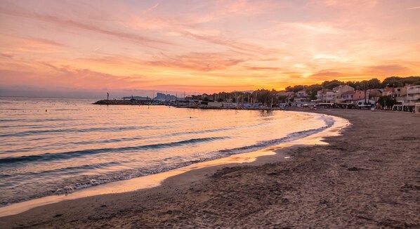 A beach with a sunset, calm waters, and a row of buildings along the shore.
