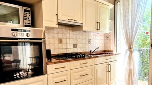 Una cocina con armarios blancos, estufa y ventana con cortina.
