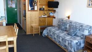 A small, cozy room with a wooden table, a sofa, a TV mounted on the wall, and a green door. - Cozy studio 3 pers. at ski slopes with Wifi (Les Arcs 1800)