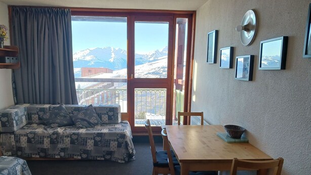 A room with a sofa, dining table, chairs, and a view of mountains through a large window. - Cozy studio 3 pers. at ski slopes with Wifi (Les Arcs 1800)
