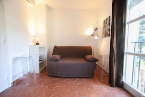 A small, cozy room with a brown sofa, a clear glass table, and a window with a view.