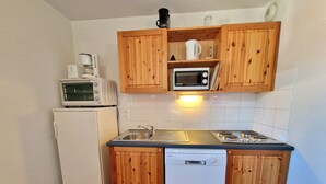 Een compacte keuken met houten kastjes, een witte koelkast, een magnetron, een koffiezetapparaat en een vaatwasser.