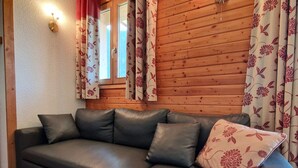 Een moderne woonkamer met een donker leren bank, bloemen gordijnen en een houten wand.