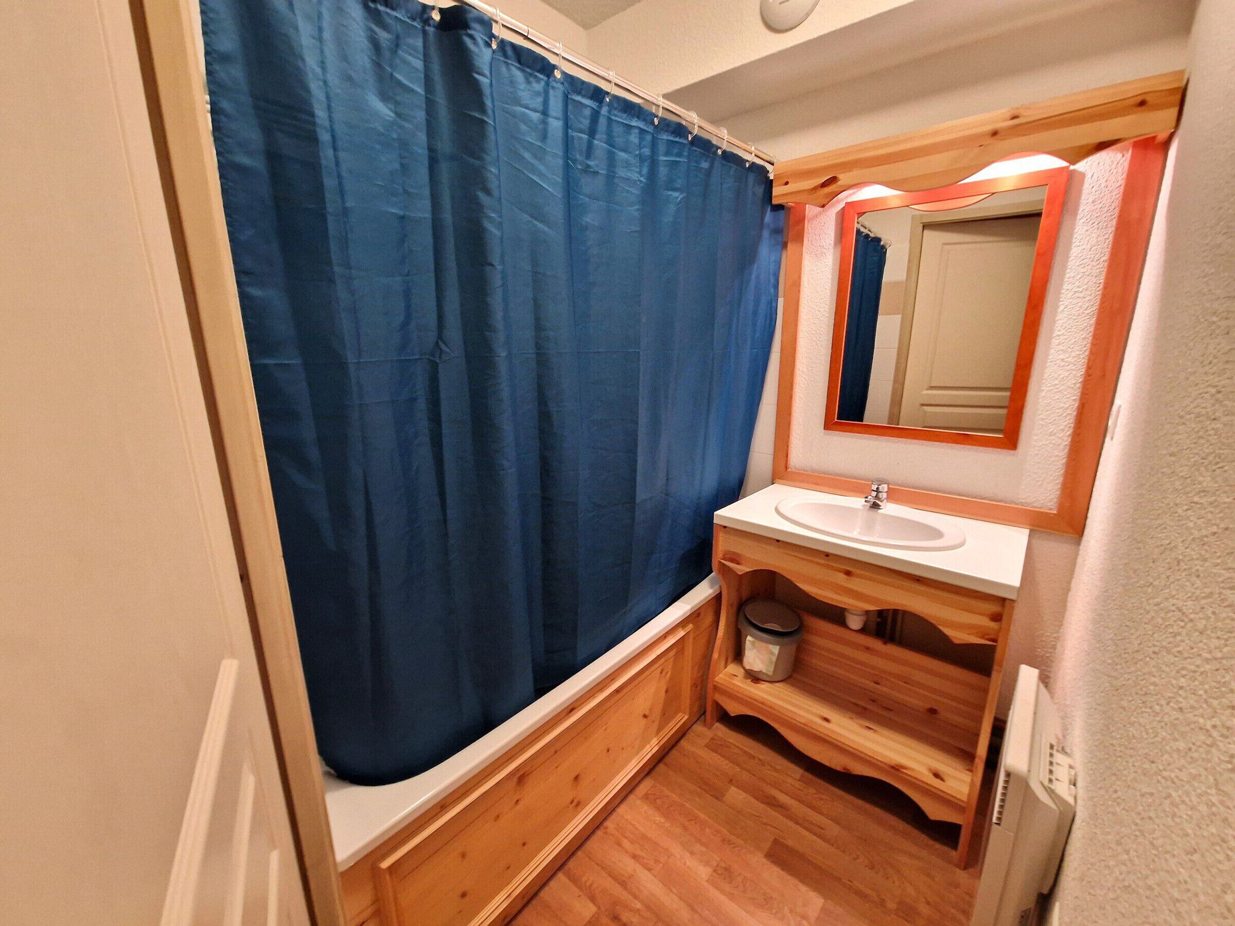 A small, compact bathroom with a wooden vanity, a white sink, a mirror, and a blue shower curtain.