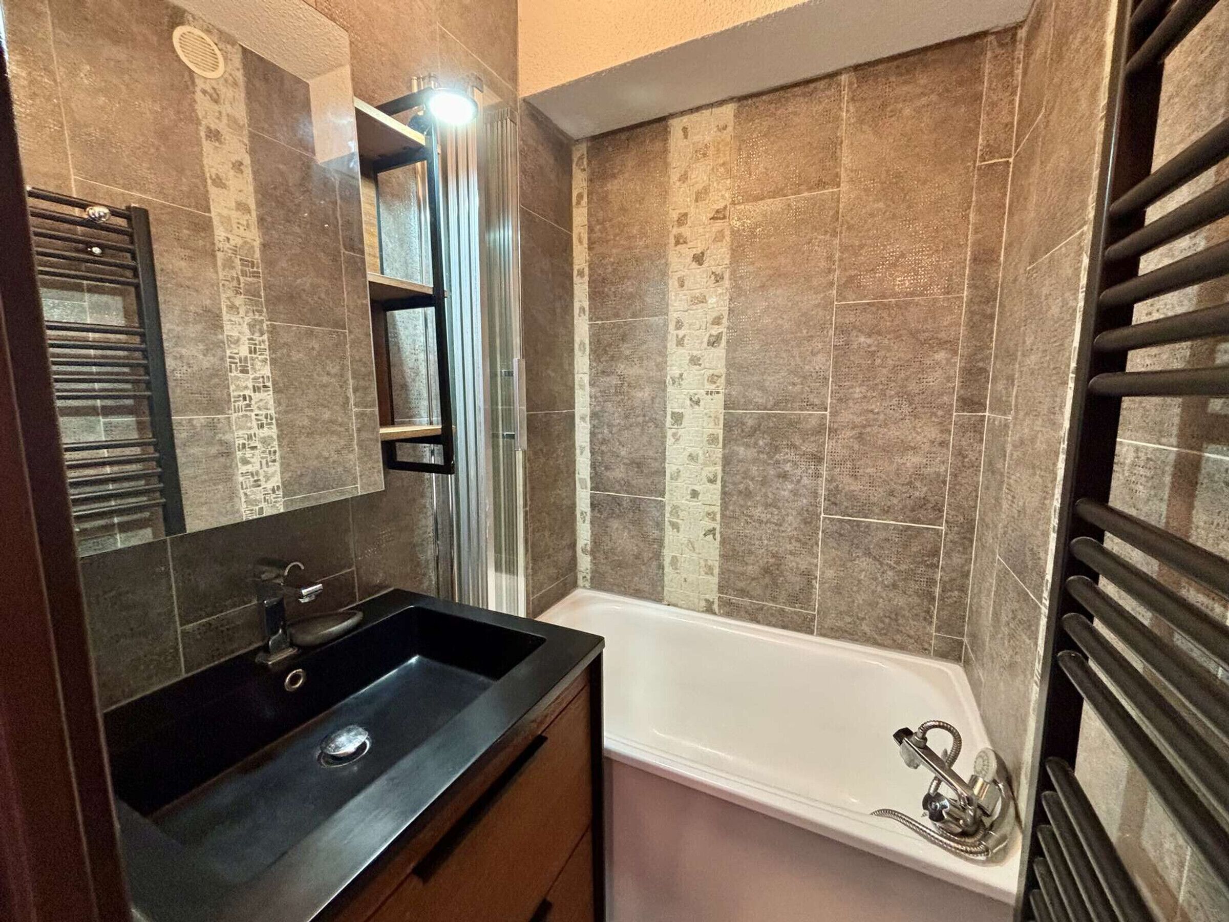 A bathroom with a black sink, a mirror, a shower, and a tiled wall.