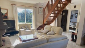 Ein geräumiges Wohnzimmer mit einer großen Couch, einem Couchtisch und einem Fernseher. Eine Holztreppe führt zu einem anderen Raum.