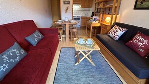 A cozy living room with a red sofa and a black sofa, a wooden dining table, and a kitchen in the background. - Méribel: Cozy 2-Room Apt, 4 Pax, near Shops and Slopes (Méribel)