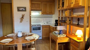 A compact kitchen with wooden cabinets, a stove, and a dining area set for four. - Méribel: Cozy 2-Room Apt, 4 Pax, near Shops and Slopes (Méribel)