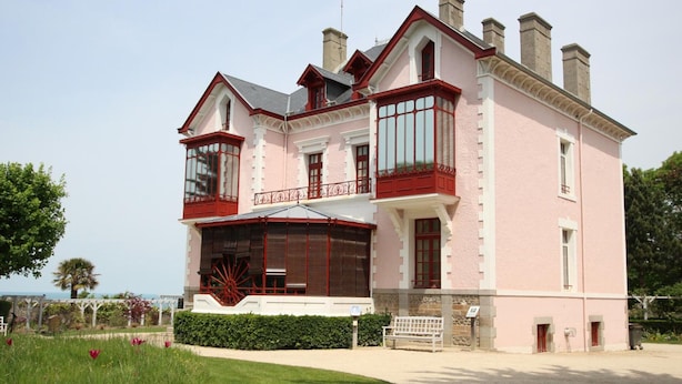 Um edifício rosa com varanda, uma janela grande e guarda-corpo vermelho.