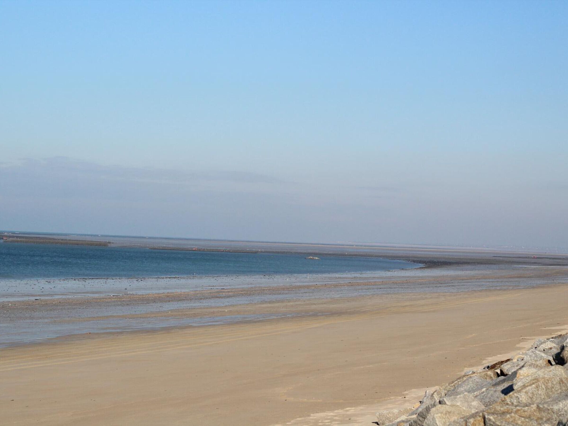 A wide sandy beach with calm water and a clear sky.