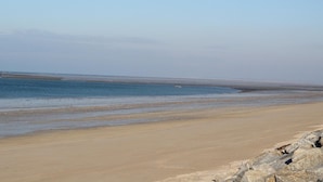 Uma extensa praia arenosa com águas calmas e céu claro.