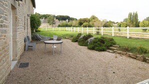 A stone building with a gravel patio, a white fence, and a view of a green field.