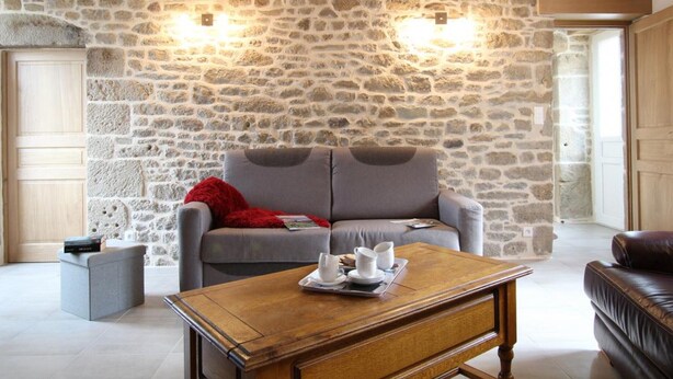 A cozy living room with a stone wall, a grey sofa, a wooden coffee table, and a leather armchair.