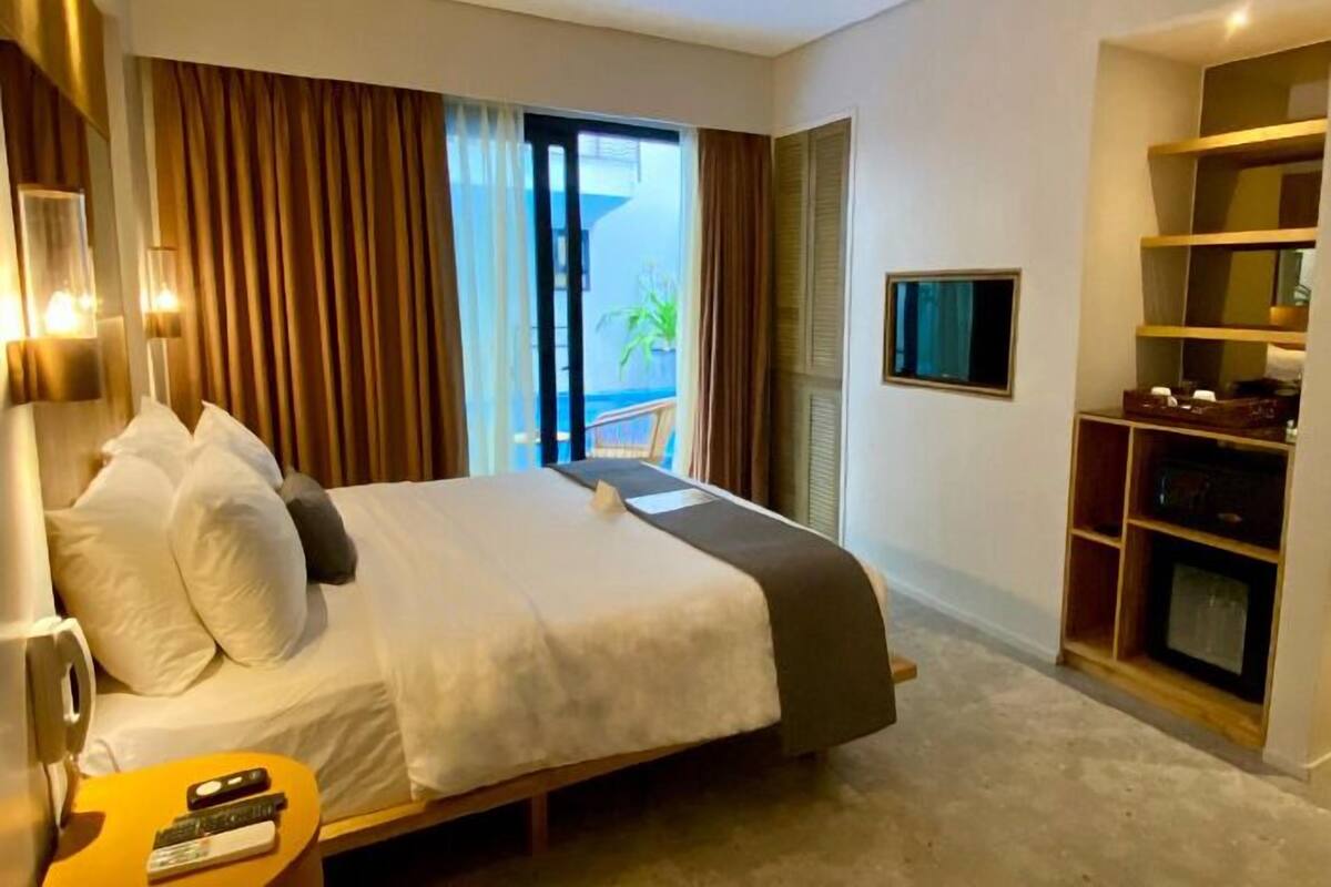 A hotel room with a bed, a TV, a desk with a lamp, and a view of the outdoors.