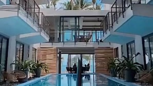 Een modern hotel met een centraal gelegen zwembad, meerdere balkons en palmbomen.
