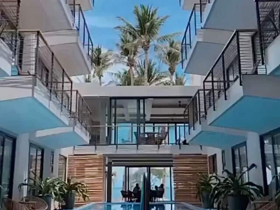 A modern hotel with a central swimming pool, multiple balconies, and palm trees.