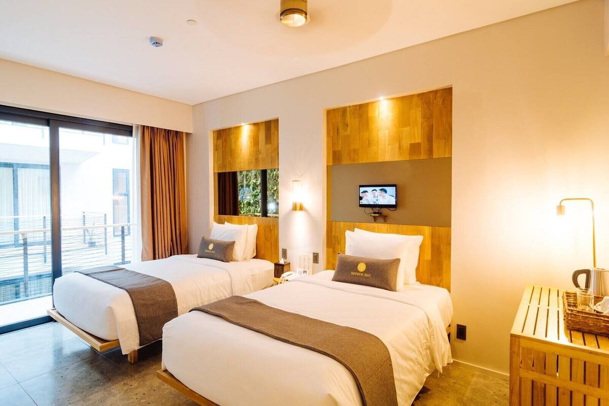 A hotel room with two beds, a TV, and a balcony with curtains.