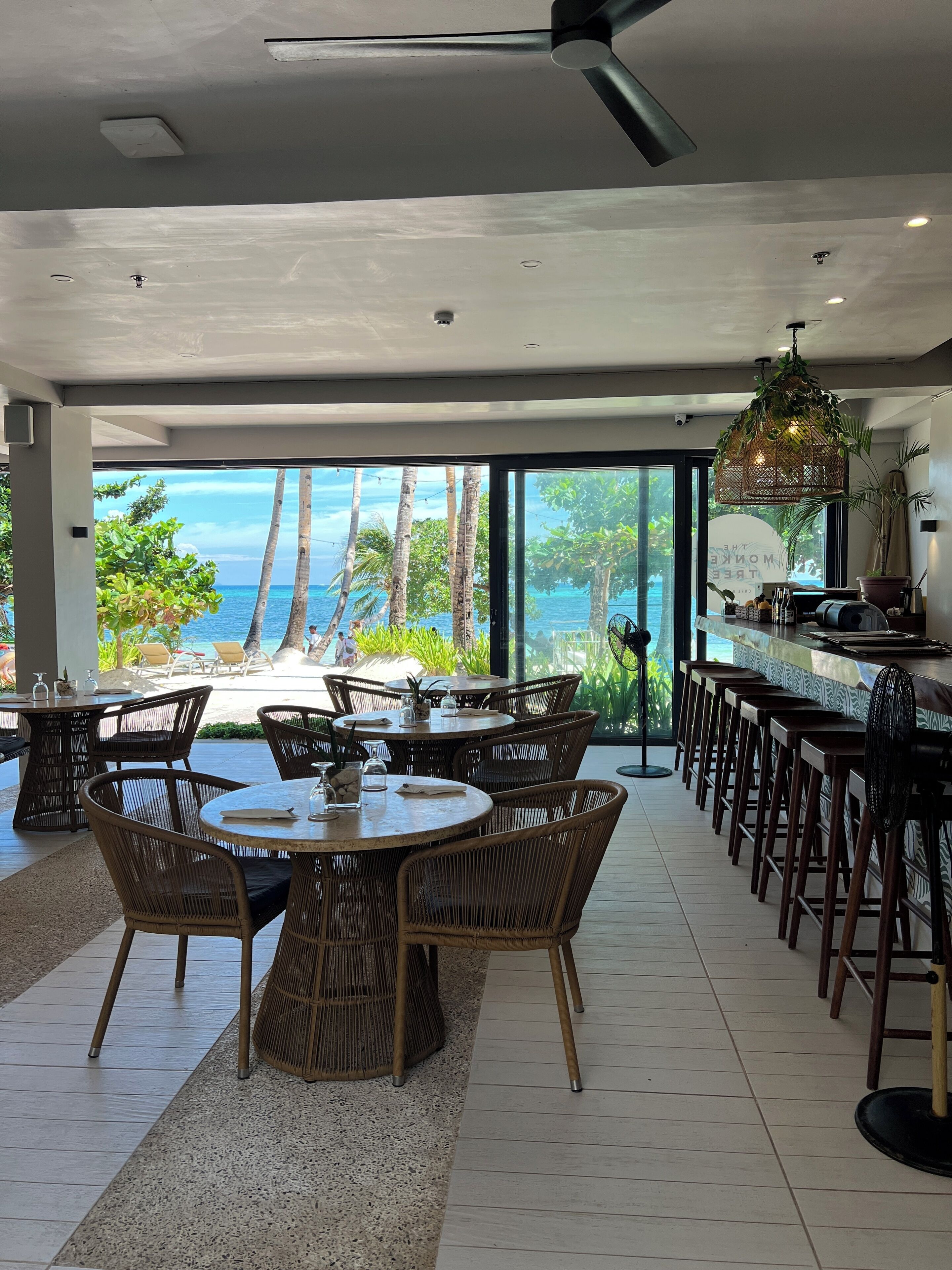 A modern interior with a bar area, dining tables, and chairs, overlooking a beach and ocean.