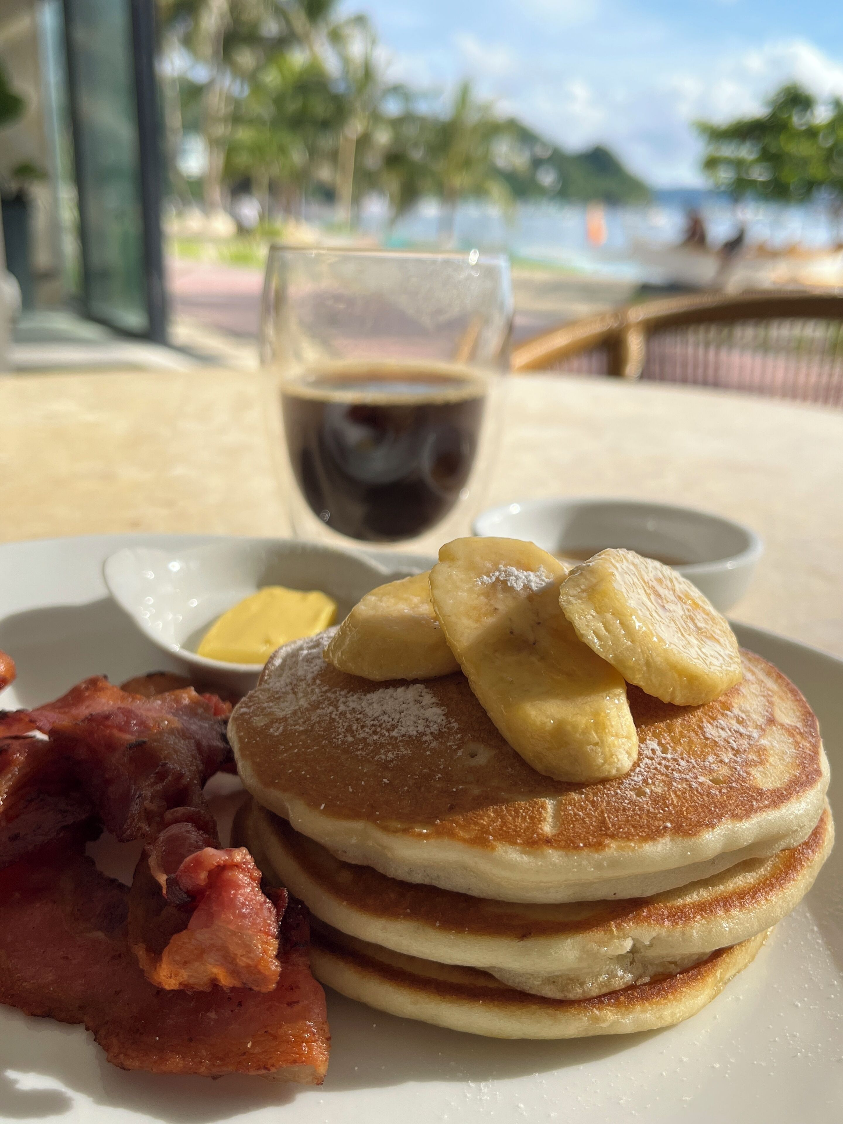 Een ontbijt bord met pannenkoeken, spek en een glas koffie.