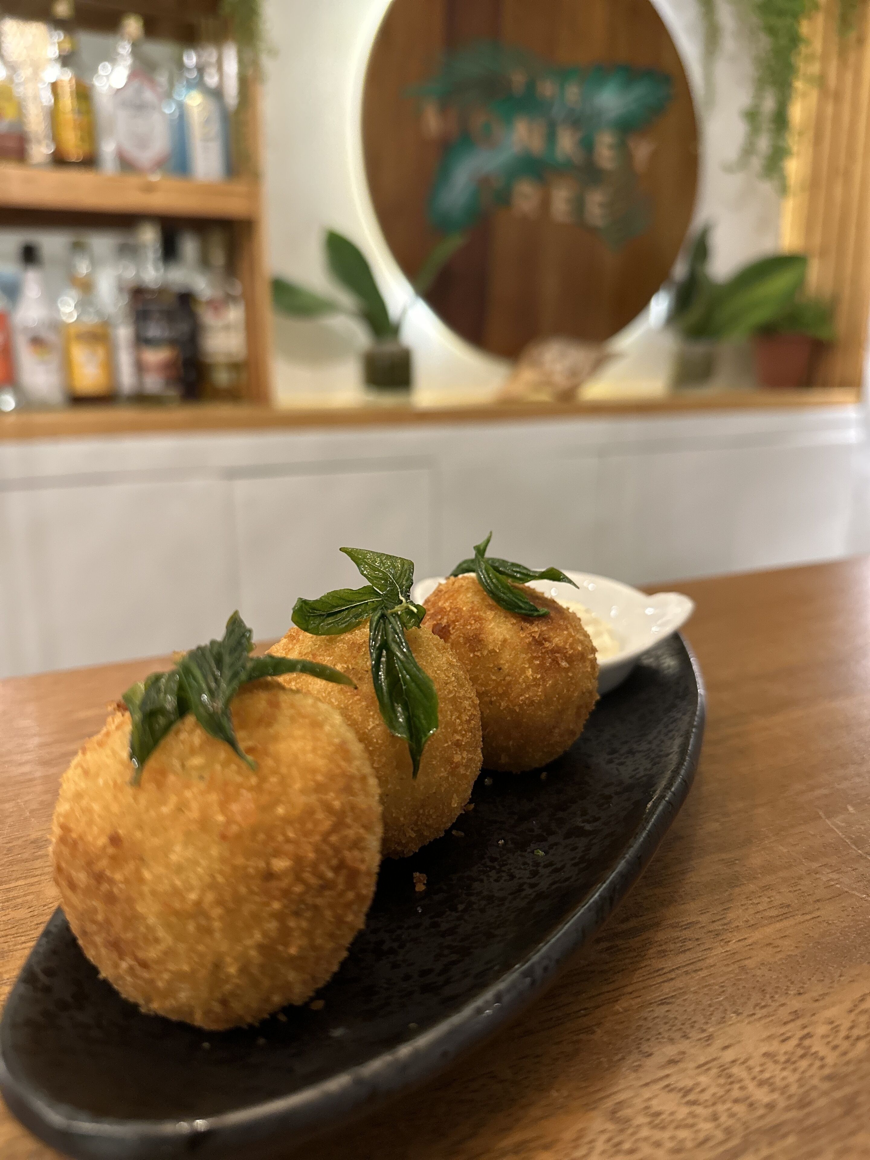 Tres piezas redondas, rebozadas, sobre un plato negro, adornadas con hojas verdes, sobre una mesa de madera.