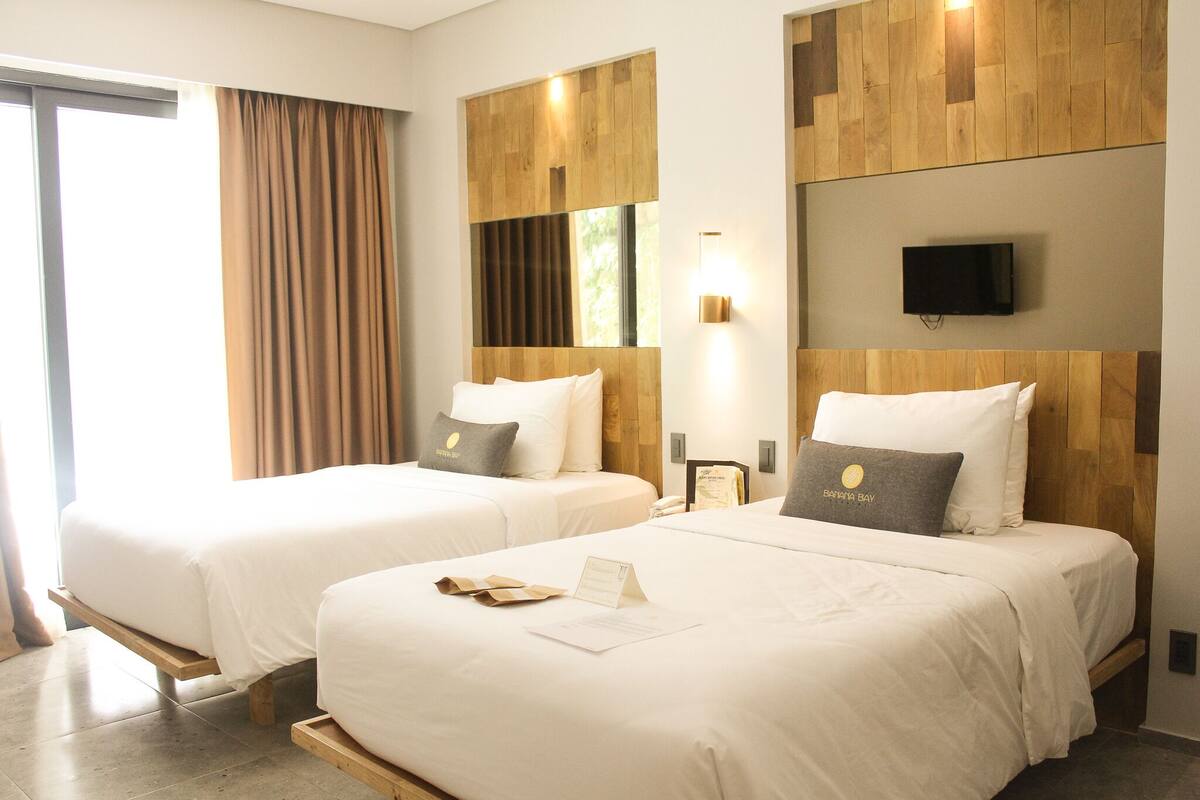 A hotel room with two beds, a TV, and a wooden wall panel.
