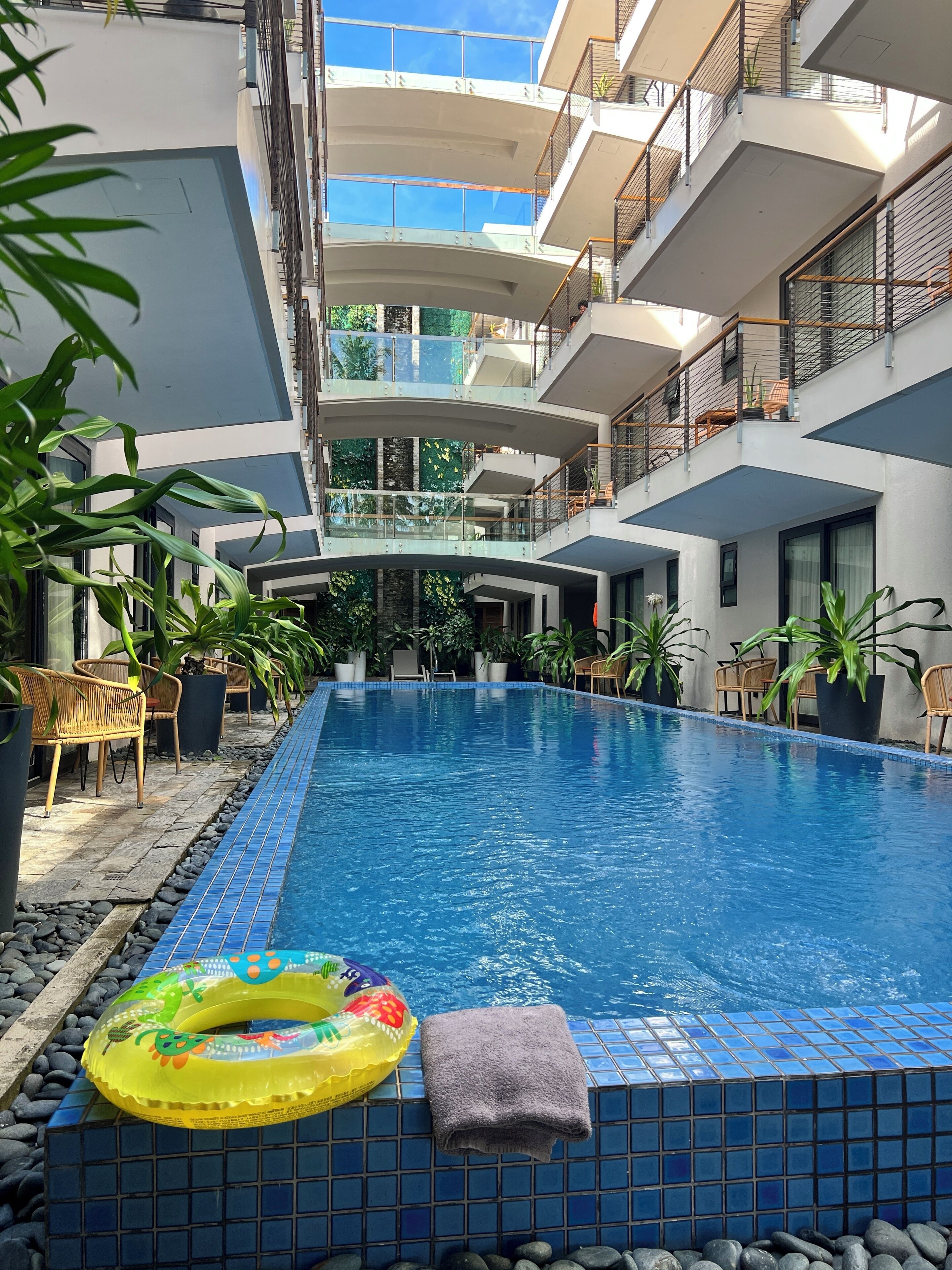 An indoor swimming pool with clear blue water, surrounded by potted plants and wicker furniture.